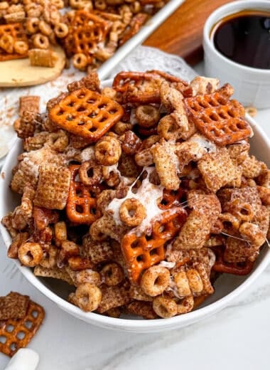 Pumpkin Spice Chex Mix in a white serving bowl with a bowl of maple syrup and cinnamon sticks