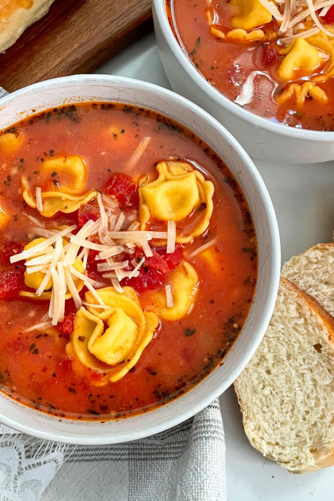 close up photo of one pot tomato tortellini soup in a white serving bowl with shredded parmesan cheese sprinkled on top