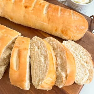 Easy 90 Minute French Bread on a cutting board. One loaf is sliced with a jar of butter in the background