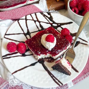 Best Chocolate Raspberry cheesecake bars recipe on a white serving plate with chocolate sauce drizzle and fresh raspberries as a garnish