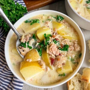 Best Olive Garden Zuppa Toscana Soup in a white serving bowl topped with bacon bits and fresh parsley.