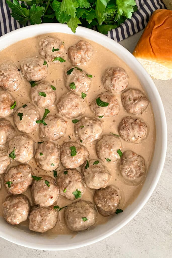 Crock Pot Swedish Meatballs in a white serving platter with rolls and fresh parsley placed behind