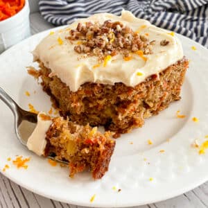 The best carrot cake with cream cheese frosting on a serving plate with a bite on a fork