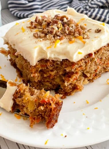 The best carrot cake with cream cheese frosting on a serving plate with a bite on a fork