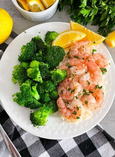 Easy oven baked shrimp on a white serving plate with steamed broccoli and sliced lemons.