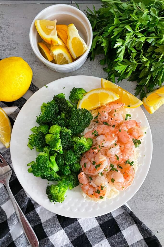 Easy oven baked shrimp on a white serving plate with steamed broccoli and sliced lemons.