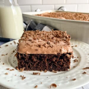skinny chocolate cake recipe with cake mix on a white serving plate. A glass of milk and pan of cake in the top of the picture