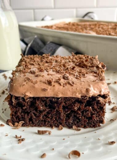 skinny chocolate cake recipe with cake mix on a white serving plate. A glass of milk and pan of cake in the top of the picture