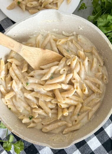creamy cottage cheese alfredo sauce served over noodles. Pictured in a large skillet with a serving plate in the top left corner