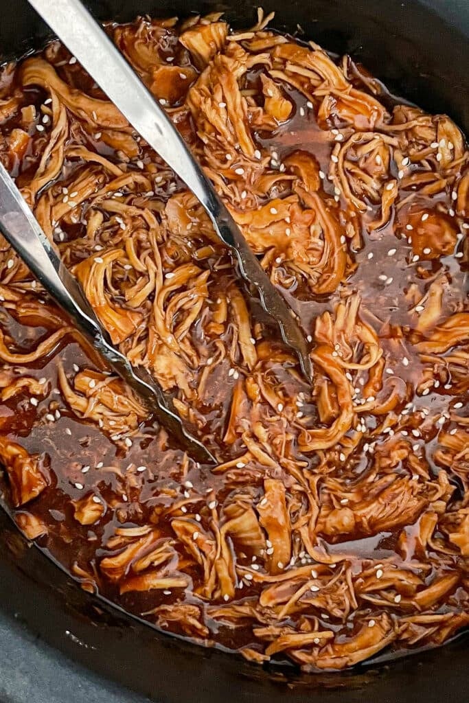 Slow cooker honey garlic chicken in a crock pot with tongs to serve