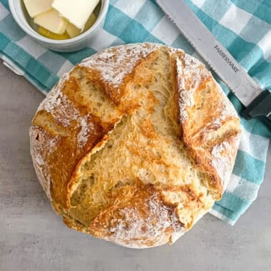 No knead easy Dutch oven bread straight out of the oven. Sliced butter and a bread knife placed in the top of the picture