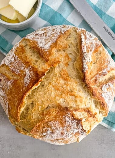 No knead easy Dutch oven bread straight out of the oven. Sliced butter and a bread knife placed in the top of the picture