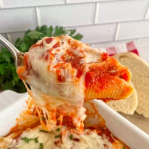Close up photo of one stuffed shell on a serving spoon held above the pan of stuffed shells