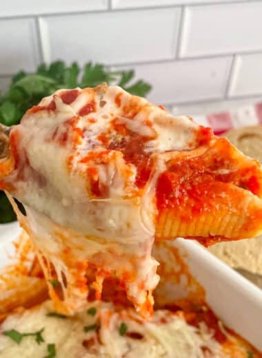 Close up photo of one stuffed shell on a serving spoon held above the pan of stuffed shells