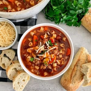 Copycat Olive Garden Pasta E Fagioli Soup in a white serving bowl with bread and parmesan cheese placed on the side.