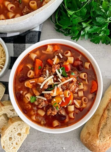 Copycat Olive Garden Pasta E Fagioli Soup in a white serving bowl with bread and parmesan cheese placed on the side.
