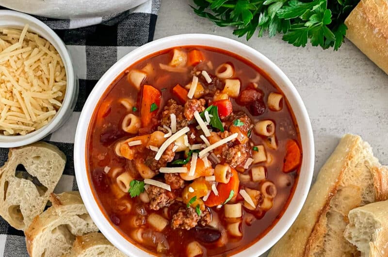Copycat Olive Garden Pasta E Fagioli Soup in a white serving bowl with bread and parmesan cheese placed on the side.