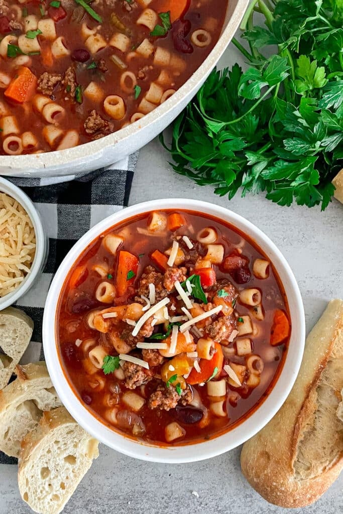 Copycat Olive Garden Pasta E Fagioli Soup in a white serving bowl with bread and parmesan cheese placed on the side.