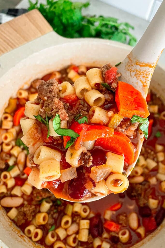 close up shot of a ladle full of pasta e fagioli soup