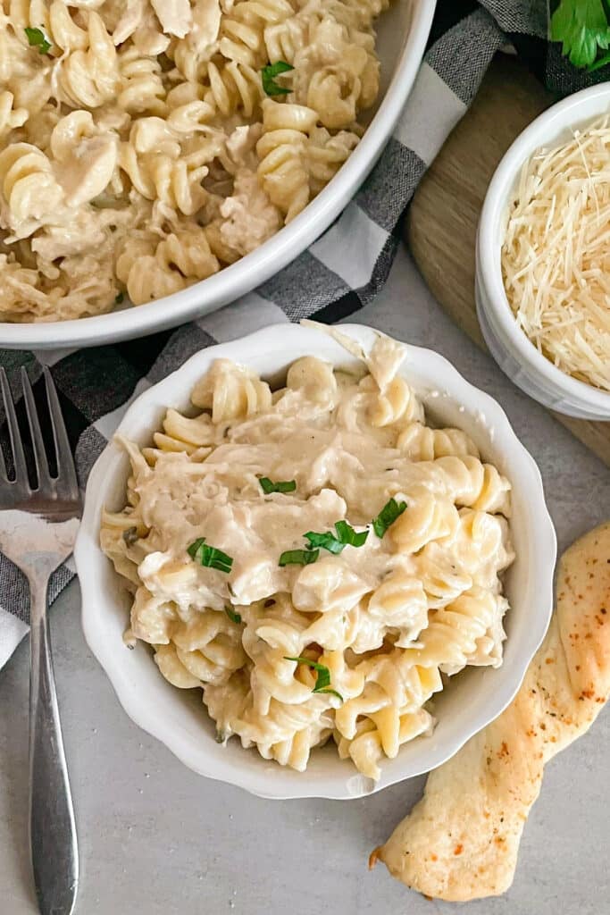 easy slow cooker garlic parmesan chicken in a sserving bowl with shredded parmesan cheese and breadstick on the side