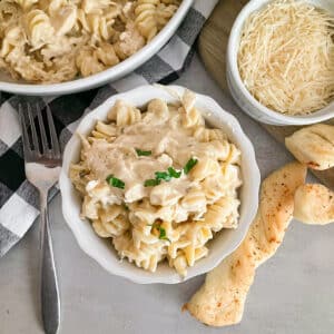easy slow cooker garlic parmesan chicken in a sserving bowl with shredded parmesan cheese and breadstick on the side