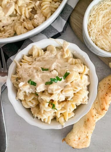 easy slow cooker garlic parmesan chicken in a sserving bowl with shredded parmesan cheese and breadstick on the side