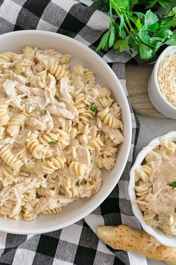 easy slow cooker garlic parmesan chicken in a sserving bowl with shredded parmesan cheese and breadstick on the side