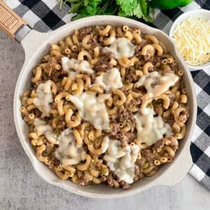 Philly cheesesteak pasta in a skillet topped with melted cheese. Parsley and shredded cheese in the top of the picture.