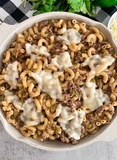 Philly cheesesteak pasta in a skillet topped with melted cheese. Parsley and shredded cheese in the top of the picture.