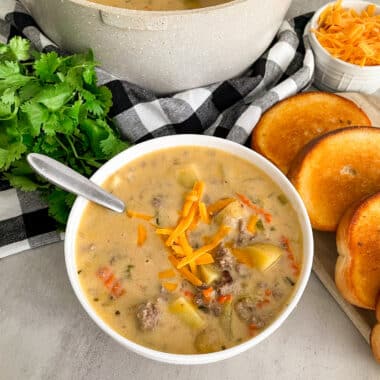 Homemade cheeseburger soup with potatoes in a serving bowl with garlic bread on the side