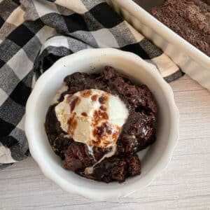 Hot fudge pudding cake in a serving bowl with a scoop of ice cream and a drizzle of fudge on top