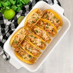 Easy baked honey lime chicken tacos in a baking dish with lime and cilantro in the upper right hand corner