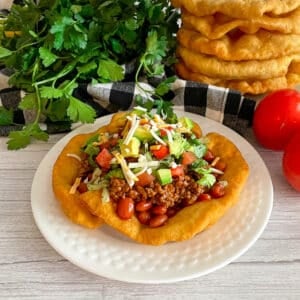 homemade Navajo taco fry bread recipe on a serving plate topped with ground beef, tomatoes, lettuce, avocado.
