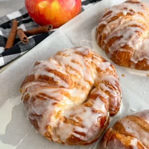 Easy apple fritter croissants baked and set on the cookie sheet. A red apple in the upper left hand corner
