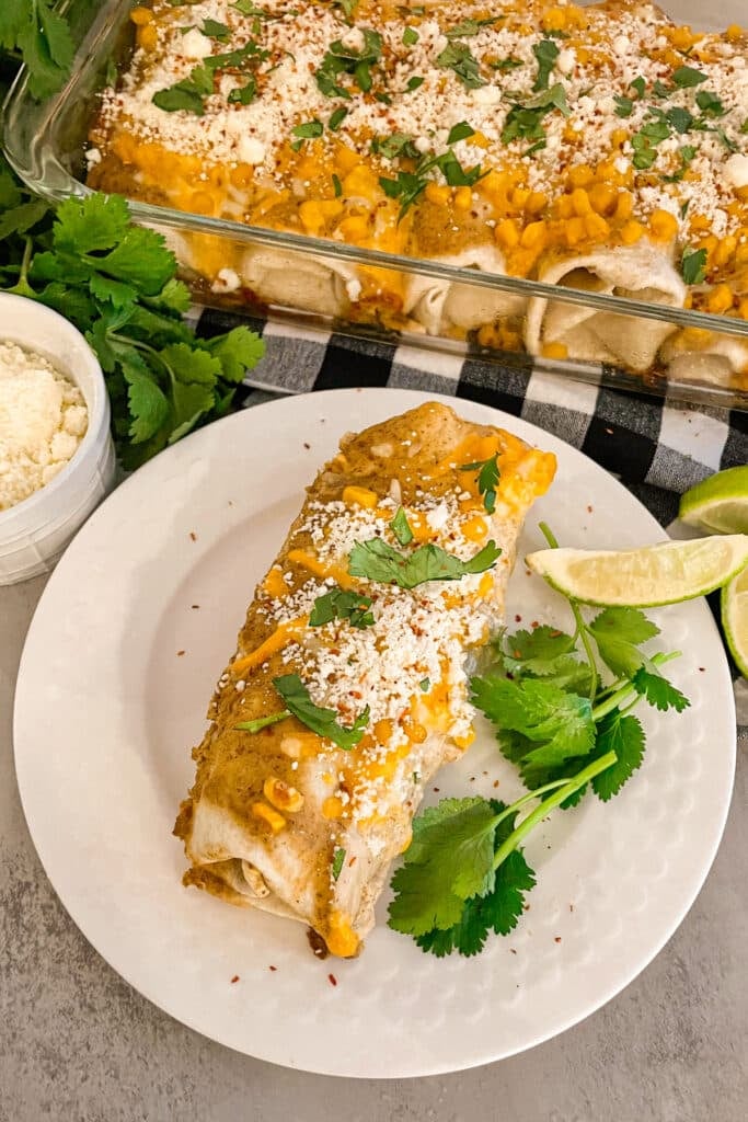 Mexican Street Corn Enchiladas on a white serving plate with the pan of enchiladas in the top right corner