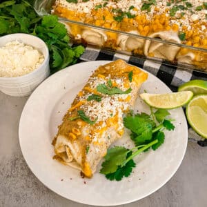 Mexican Street Corn Enchiladas on a white serving plate with the pan of enchiladas in the top right corner