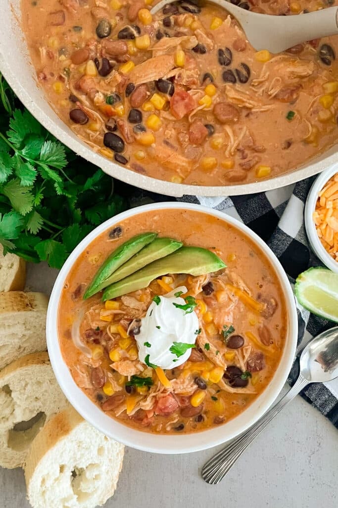 Easy Creamy Chicken Taco Soup in a white serving bowl topped with sour cream and sliced avocado