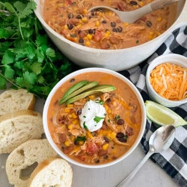 Easy Creamy Chicken Taco Soup in a white serving bowl topped with sour cream and sliced avocado