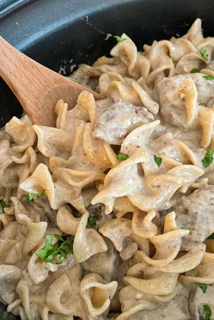 close up shot of slow cooker beef stroganoff recipe with a wooden spoon for serving