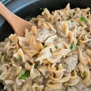 close up shot of slow cooker beef stroganoff recipe with a wooden spoon for serving