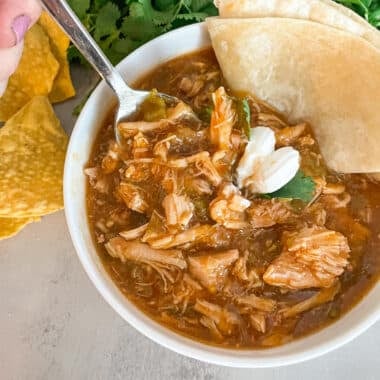 Easy slow cooker chili verde in a serving bowl topped with sour cream, fresh tortilla for dipping