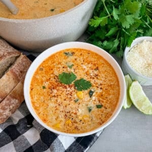 Mexican Street corn soup served in a white bowl topped with Tajin, and cilantro leaf. Pot of Soup in the upper left corner of picture.