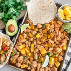 one pan pineapple chicken tacos ready to serve. Pineapple chunks and cooked tortillas shown on the sheet pan for serving