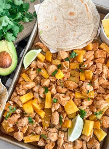 one pan pineapple chicken tacos ready to serve. Pineapple chunks and cooked tortillas shown on the sheet pan for serving
