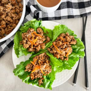 copycat P.F. changs lettuce on a white plate for serving. Peanut sauce and skillet with turkey filling on the side