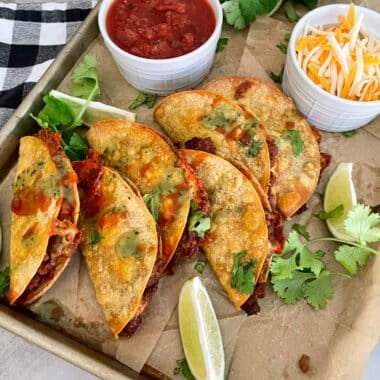 crispy oven baked tacos on a sheet pan with a side of salsa and shredded cheese