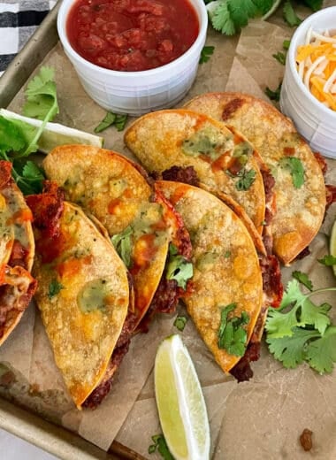 crispy oven baked tacos on a sheet pan with a side of salsa and shredded cheese