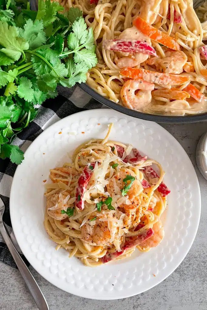 30-minute creamy Cajun shrimp pasta on a white serving plate, a fork to the left, and the skillet with pasta in the upper right hand corner of picture