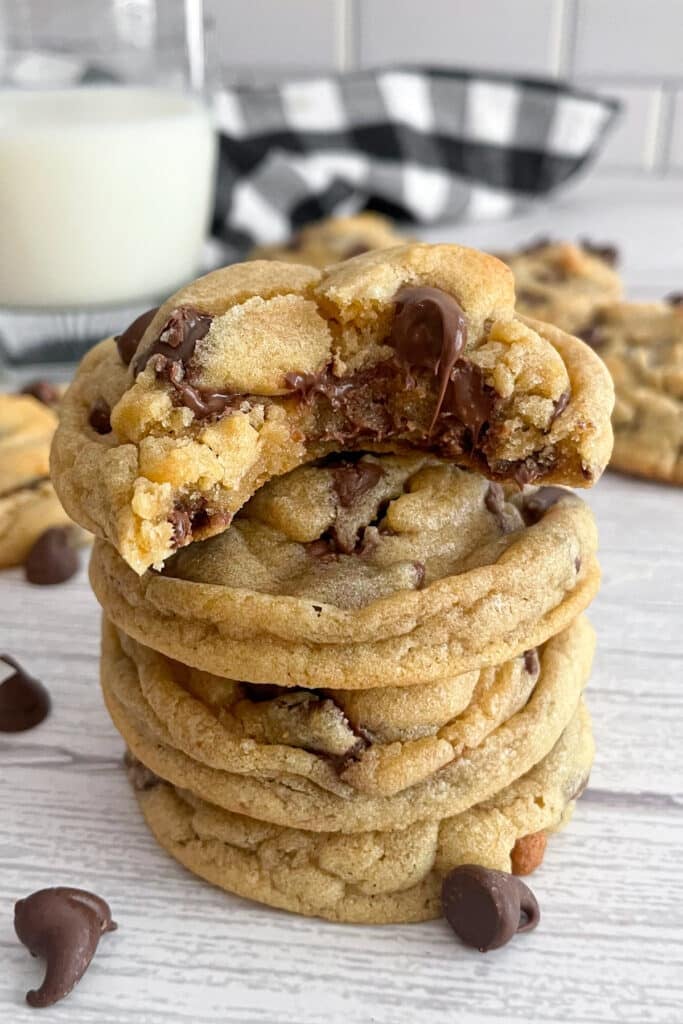 four Crumbl chocolate chip cookies stacked on top of each other. The top cookie has a bite taken out of it to show the gooey texture.