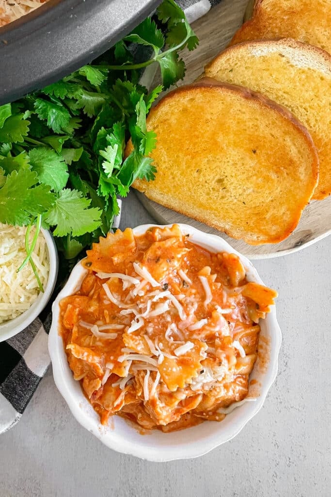 Easy crock pot Italian chicken pasta in a white serving dish with garlic bread and shredded cheese on the side